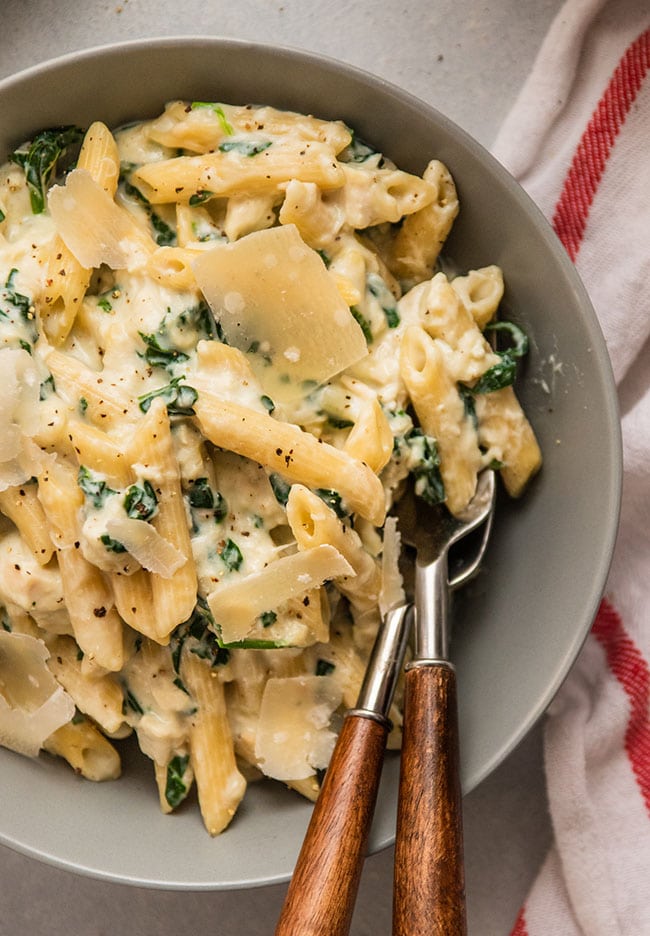 Two wooden spoons in a grey serving bowl filled with creamy penne pasta.