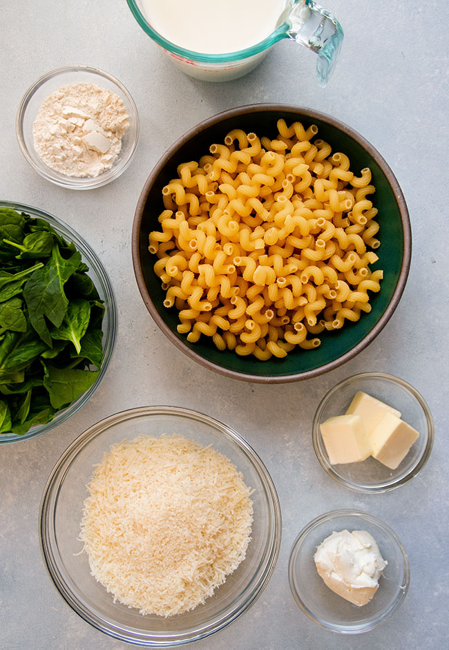 Small bowls filled with mac and cheese ingredients on a white surface.