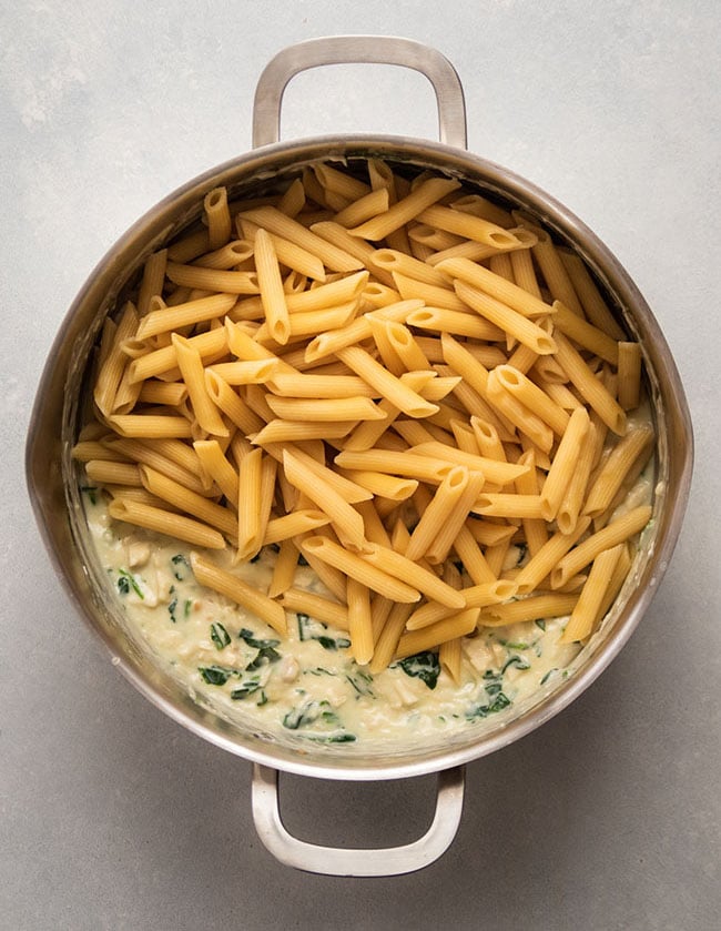 Adding cooked penne to parmesan sauce in a large pot.