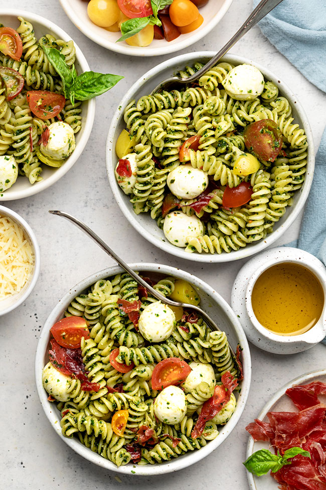 Two white bowls of caprese pasta salad on a white table.