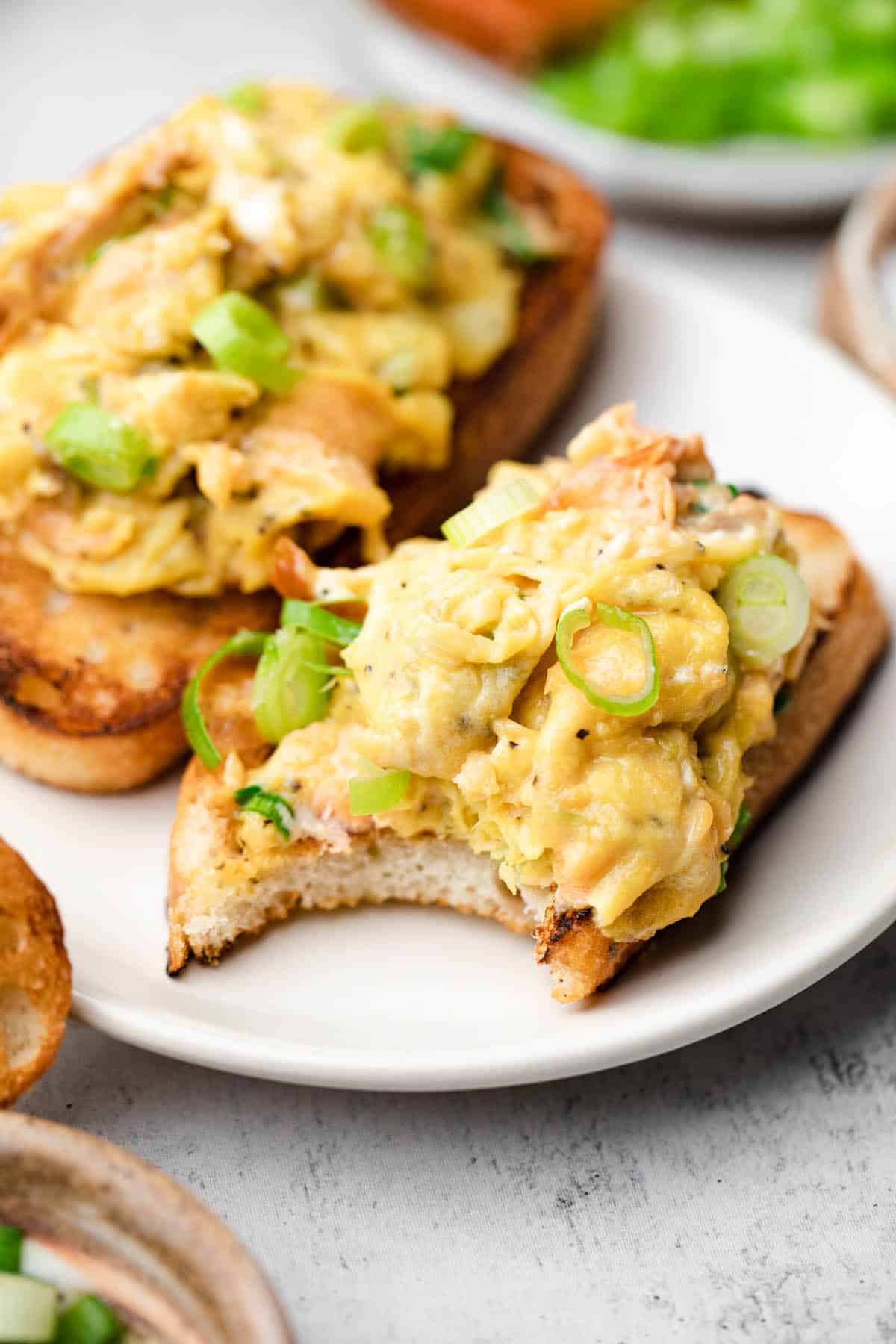 Scrambled eggs on a piece of toast with a bite taken out of it.