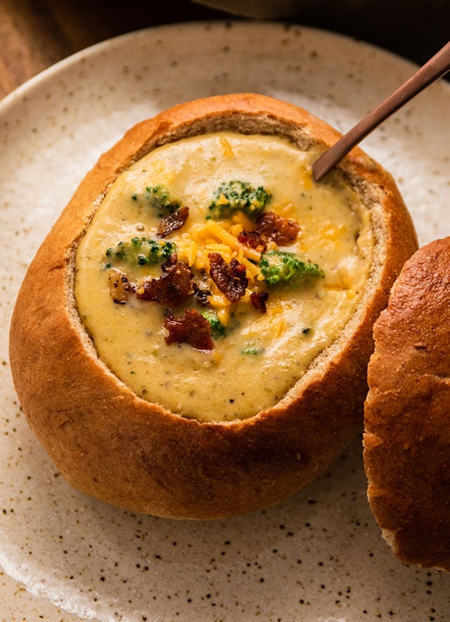 Broccoli cheddar soup in a bread bowl with a copper spoon.