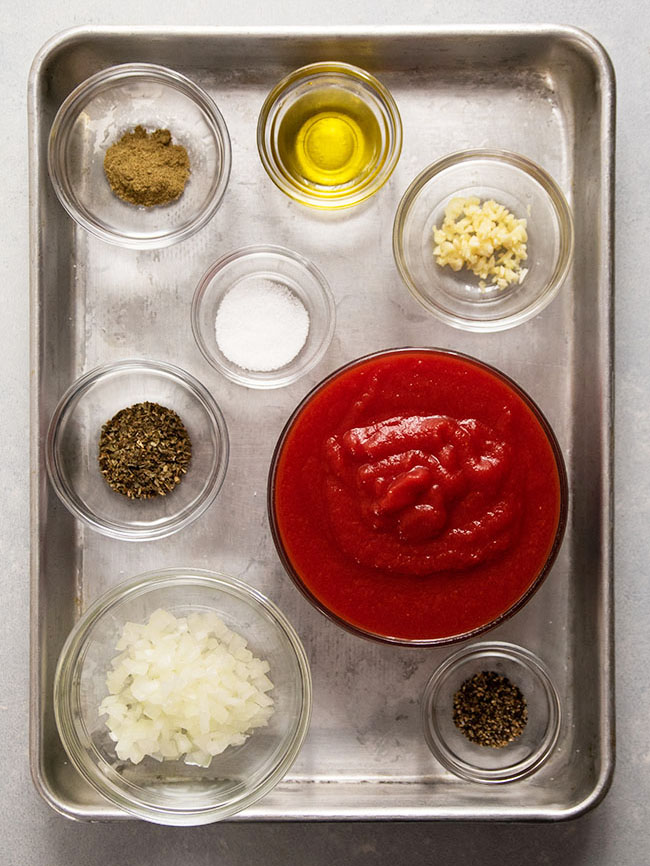 Pizza sauce ingredients in small glass bowls on a metal baking sheet.