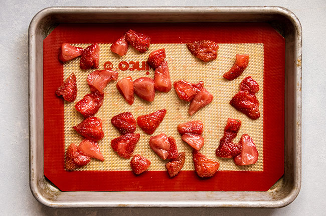 Cooked strawberries on a sheet pan lined with a nonstick baking mat, ready to freeze for smoothies.