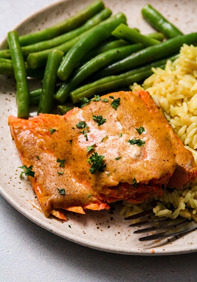 A piece of mustard salmon on a plate with green beans and rice pilaf.