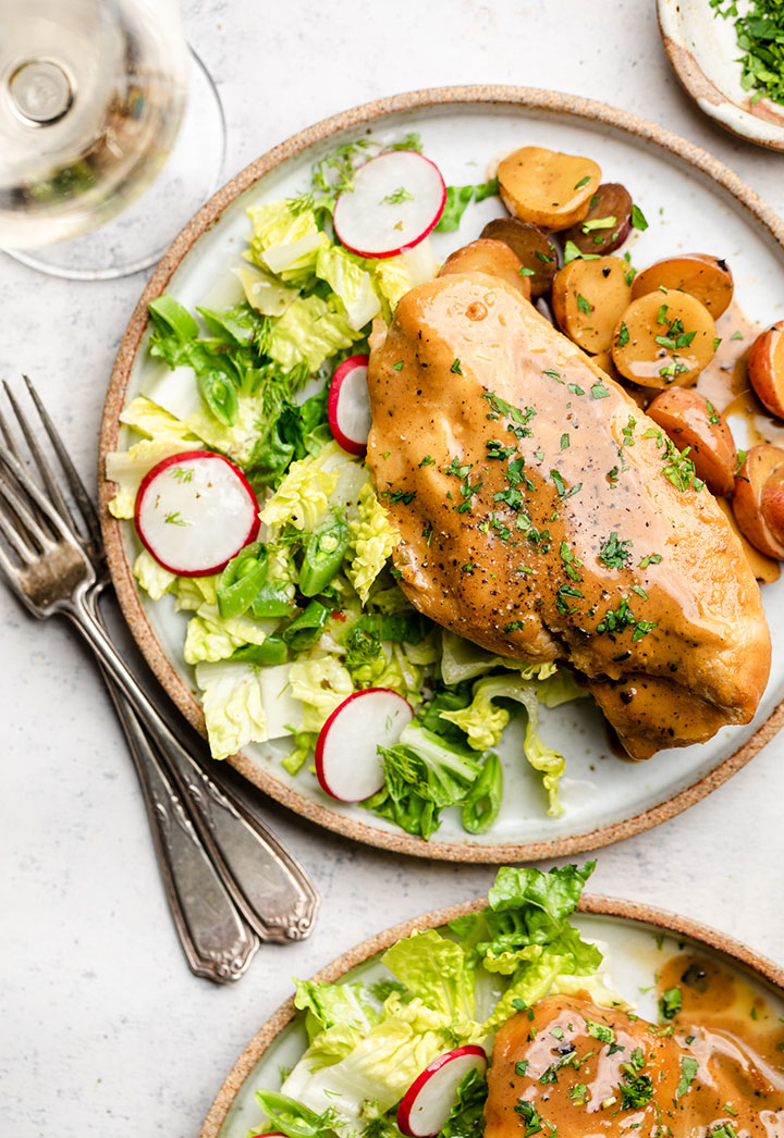 Dijon chicken on a white plate with roasted potatoes and salad.