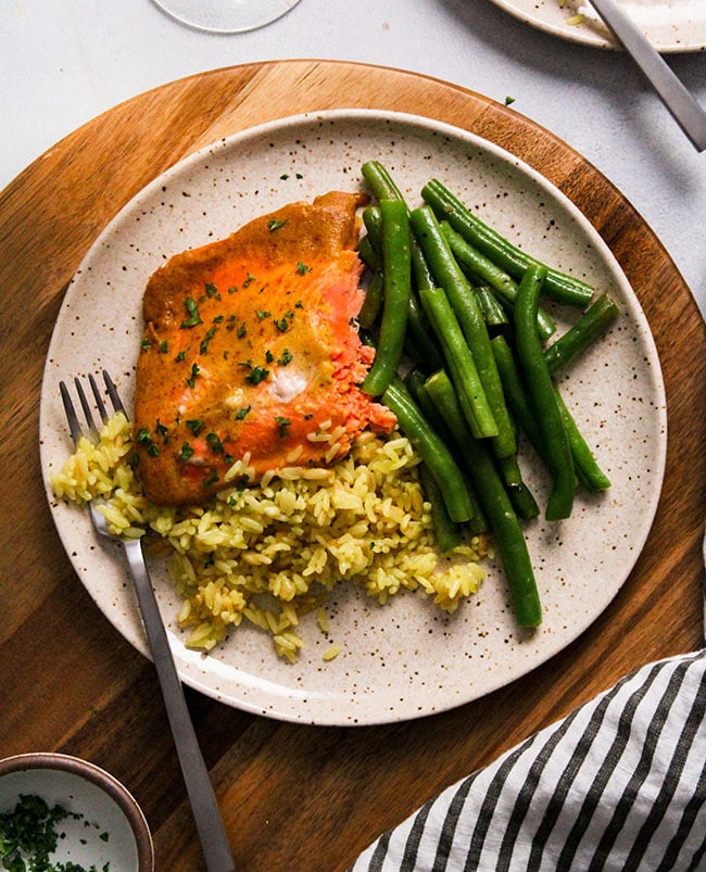 Overhead view of a piece of mustard salmon on a tan plate with green beans and rice.
