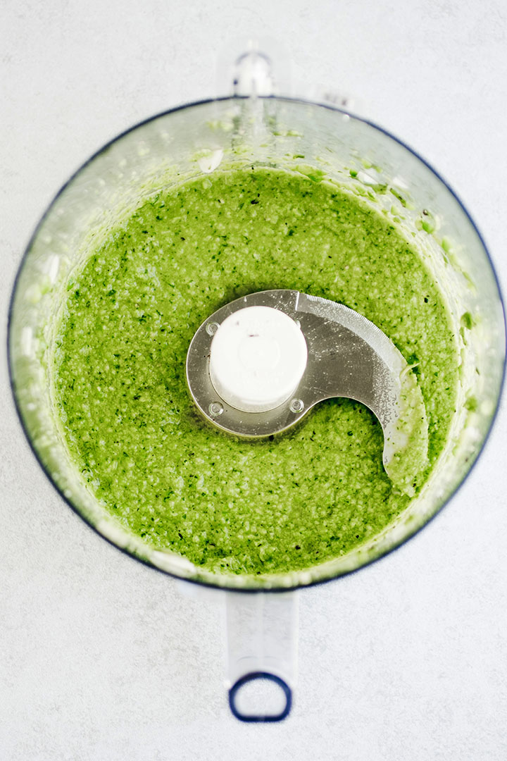 Bright green pesto in the bowl of a food processor.