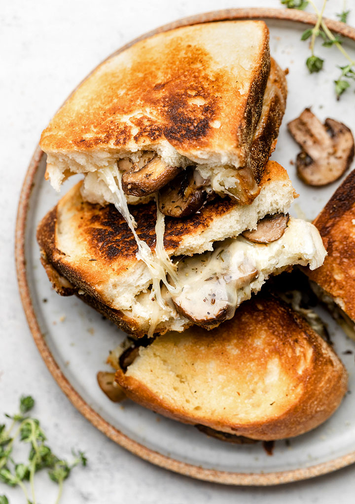 Three mushroom grilled cheese sandwiches stacked on a light grey plate.