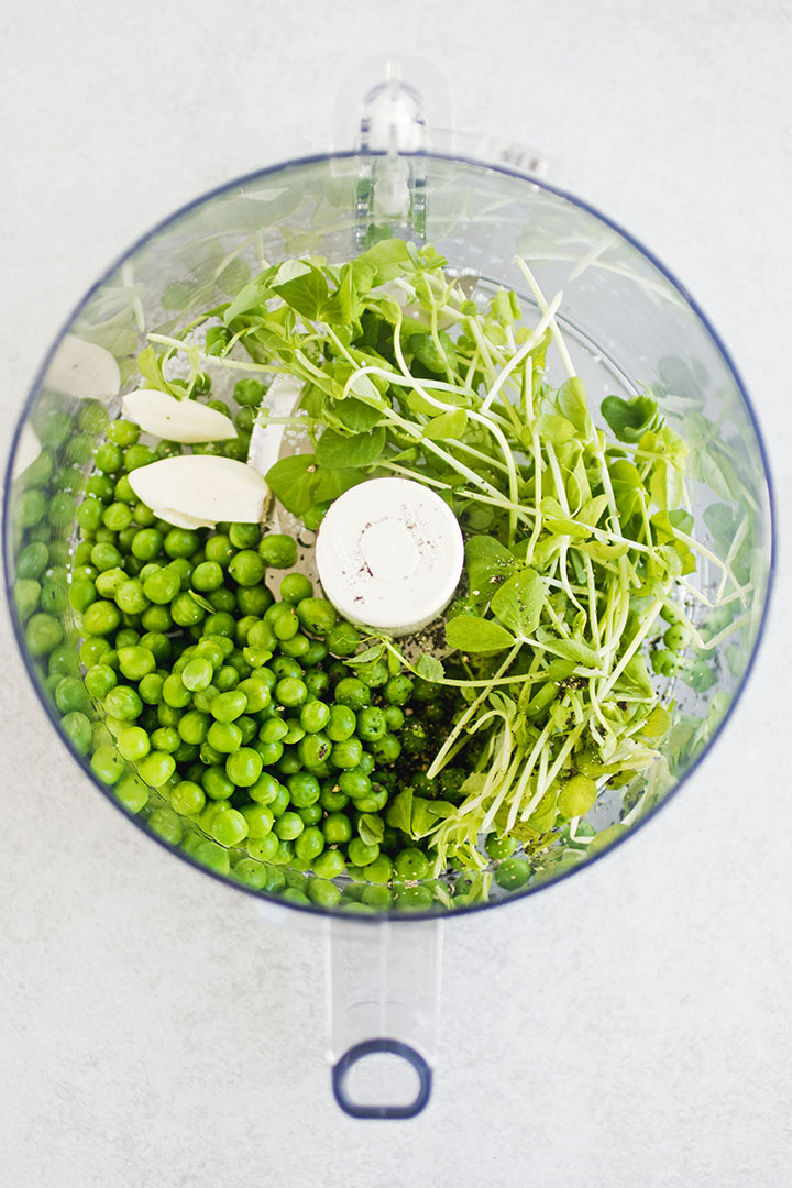 Peas, pea shoots, and garlic in the bowl of a food processor.
