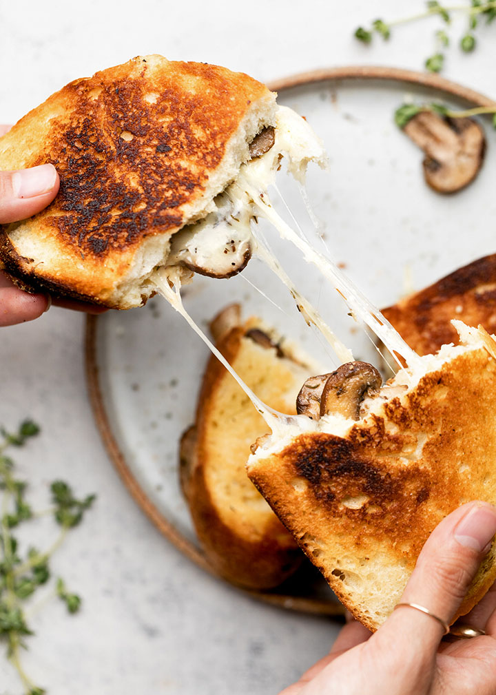 Hands pulling two halves of a grilled cheese sandwich apart as melted mozzarella stretches out.