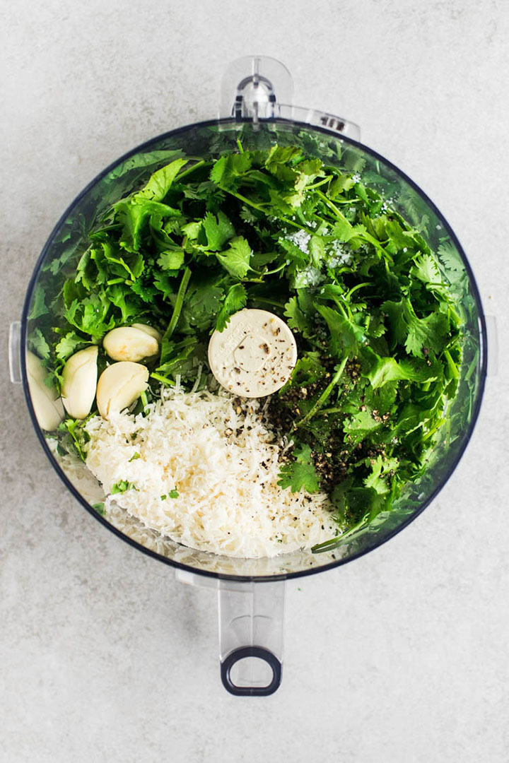 Cilantro, garlic, and parmesan in the bowl of a food processor.