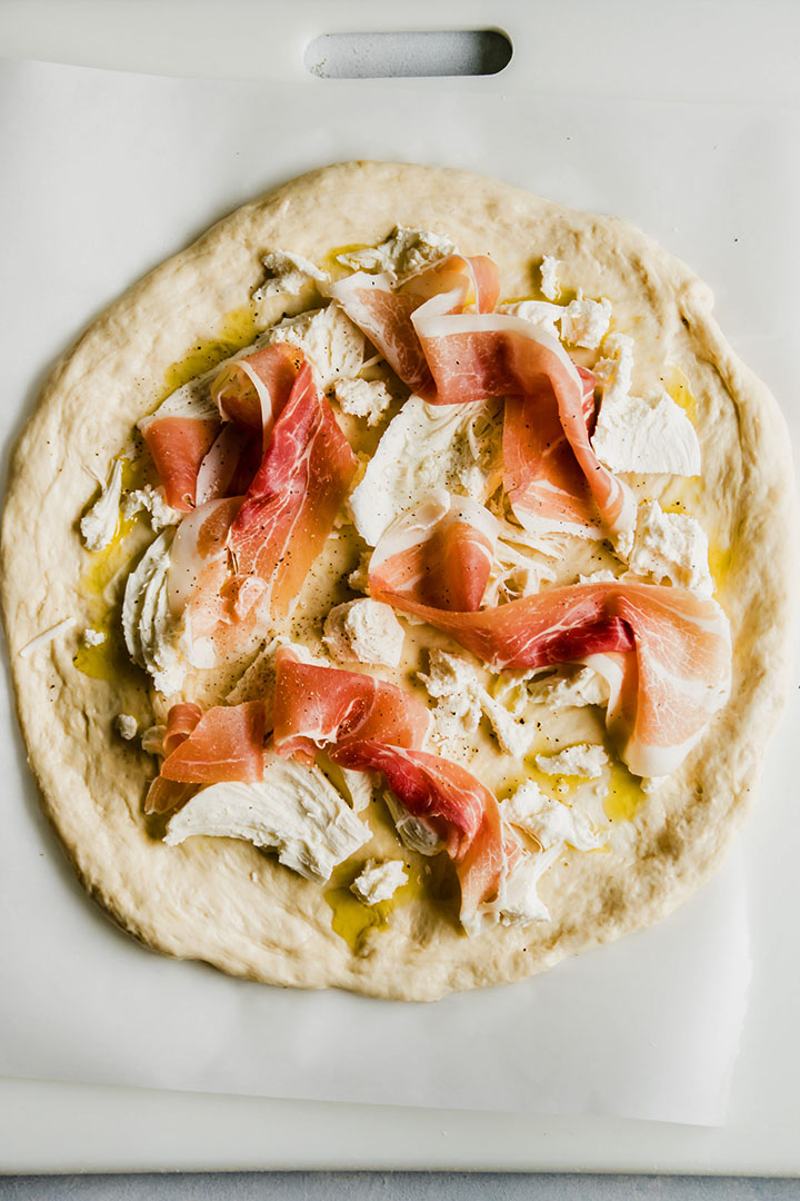 Fresh mozzarella and sliced prosciutto on top of pizza dough.