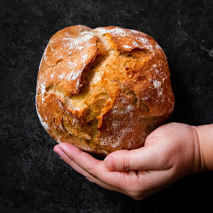 Hand holding a small loaf of bread in front of a black background.