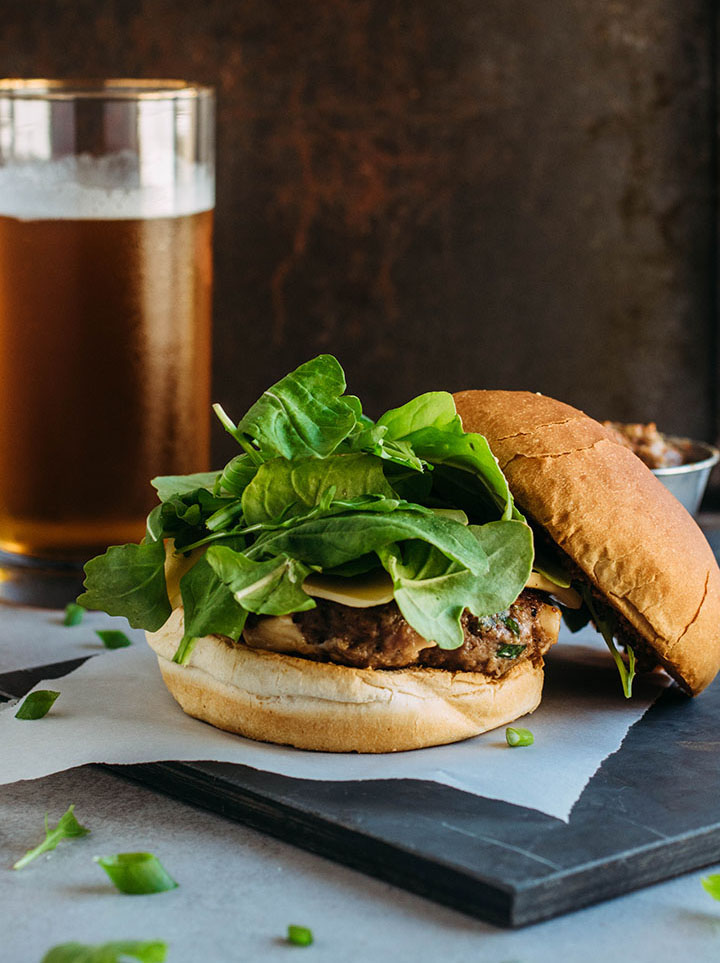 Cheeseburger topped with fresh arugula, with the top bun off to the side.