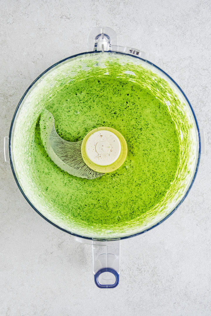 Bright green dressing in the bowl of a food processor.