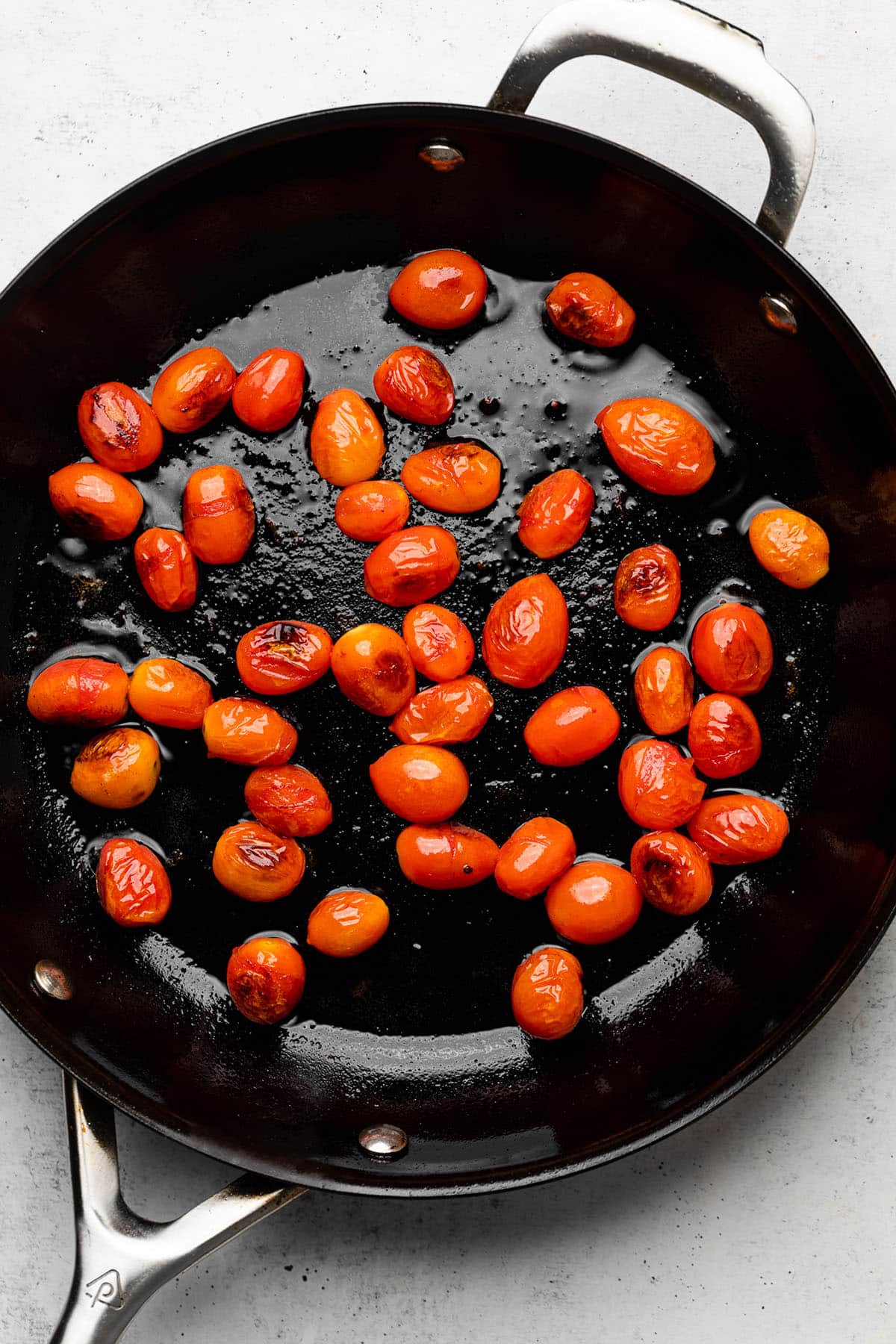 Cooking cherry tomatoes in a cast iron skillet until they begin to burst.