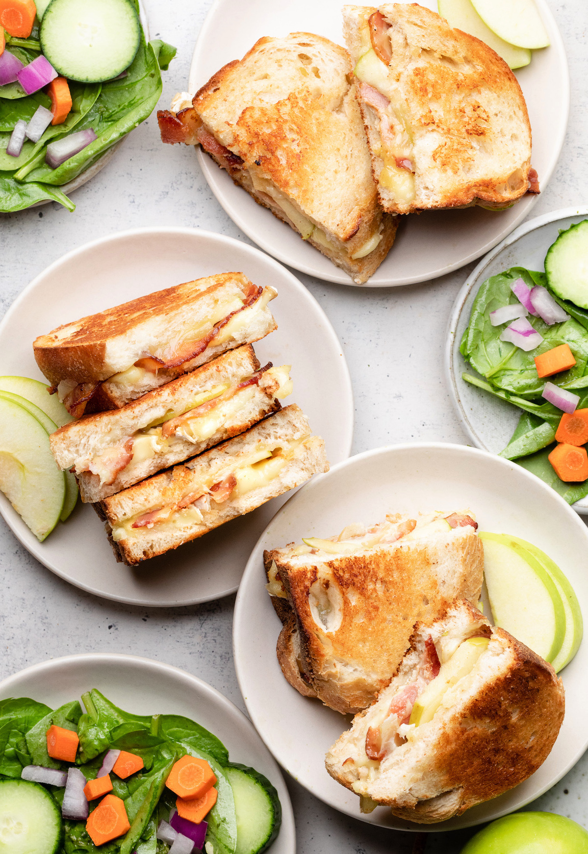 Three grilled cheese sandwiches on small white plates, next to small bowls of green salad.