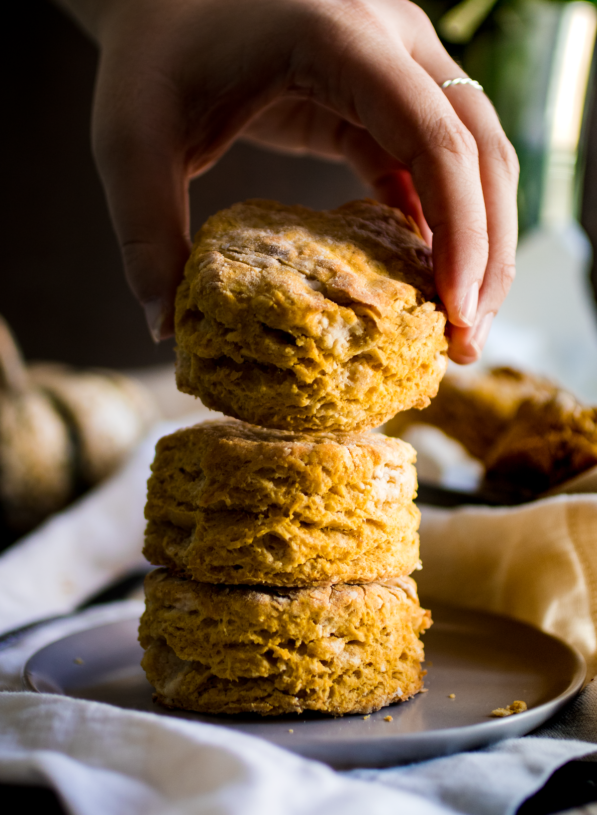Woman's hand placing a pumpkin biscuit on top of two other biscuits to form a stack.
