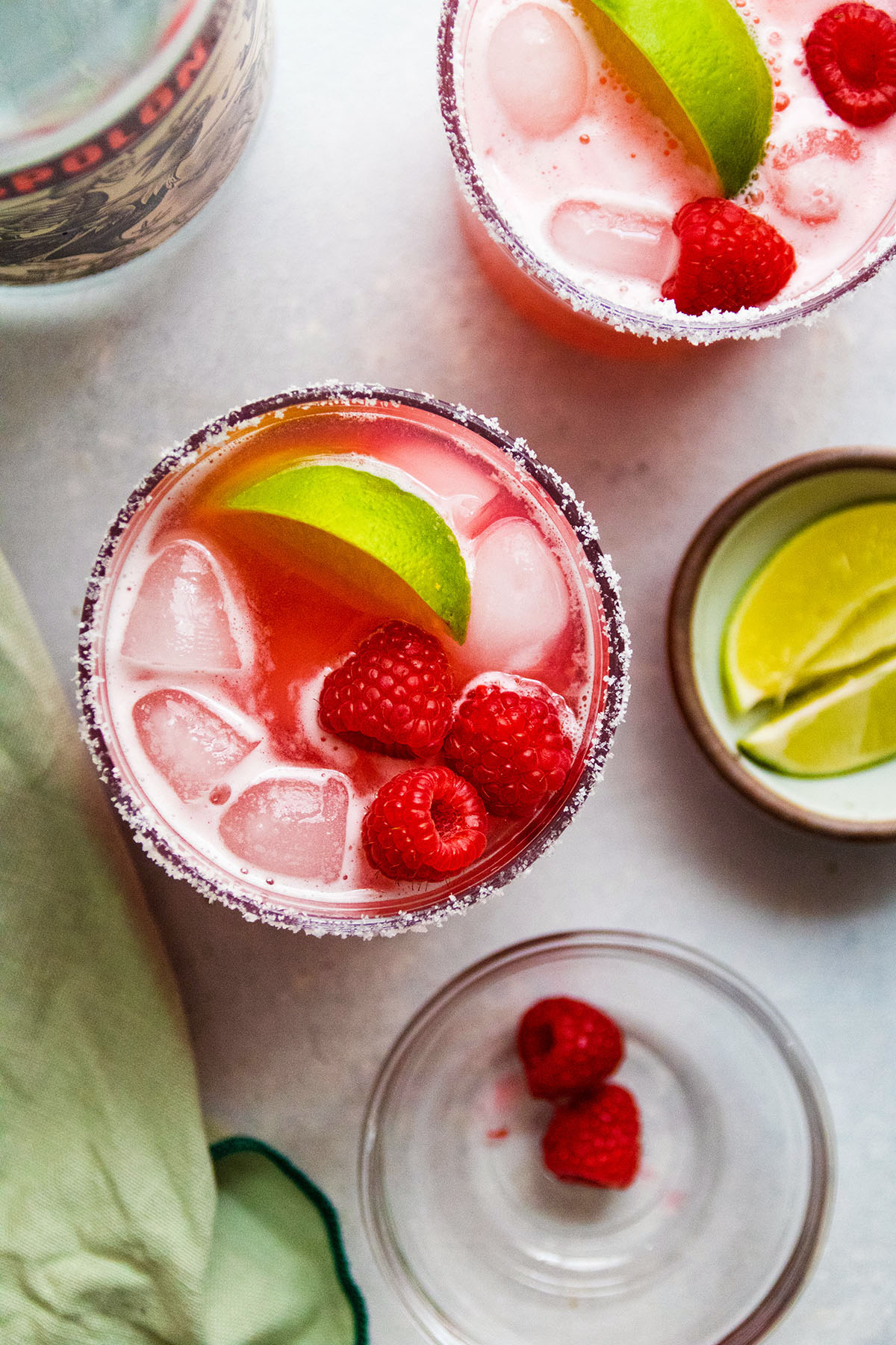 Overhead view of two margaritas next to a bowl of fresh raspberries and a bowl of lime wedges.