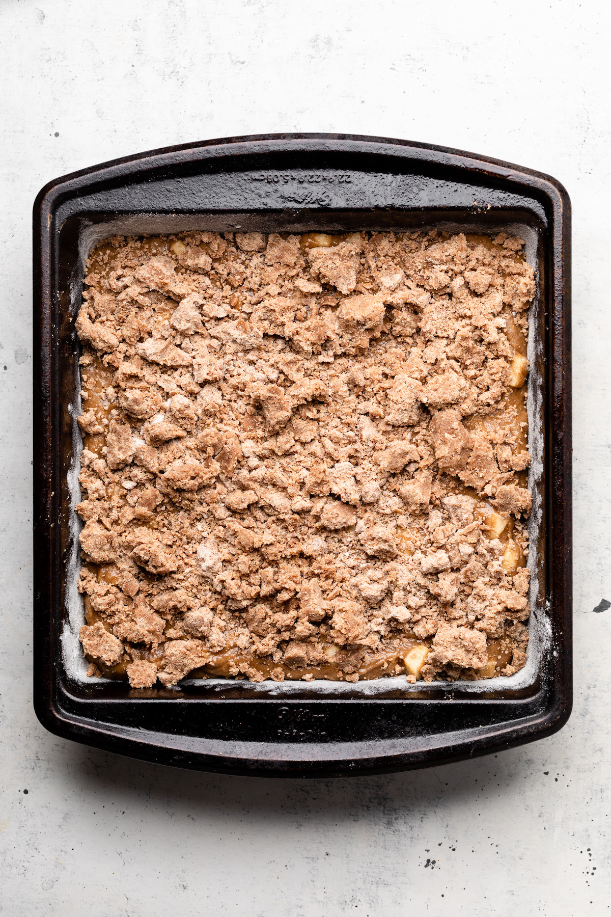 Coffee cake batter in a dark, square baking dish, topped with crumble topping.