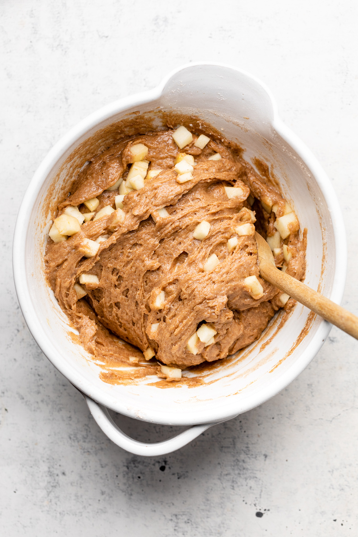 Wooden spoon stirring diced apples into coffee cake batter.