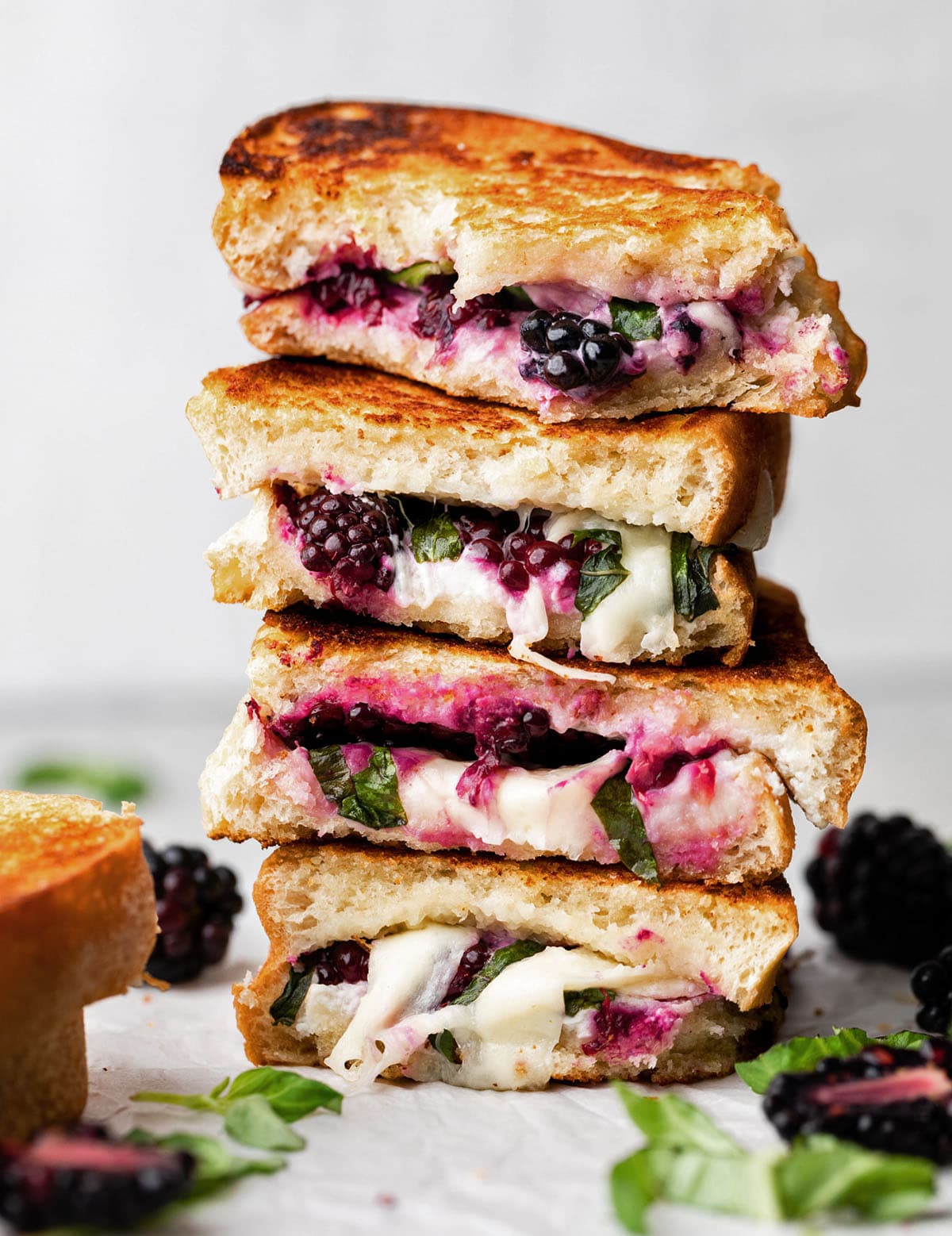 Four blackberry grilled cheese sandwiches in a stack in front of a white wall.