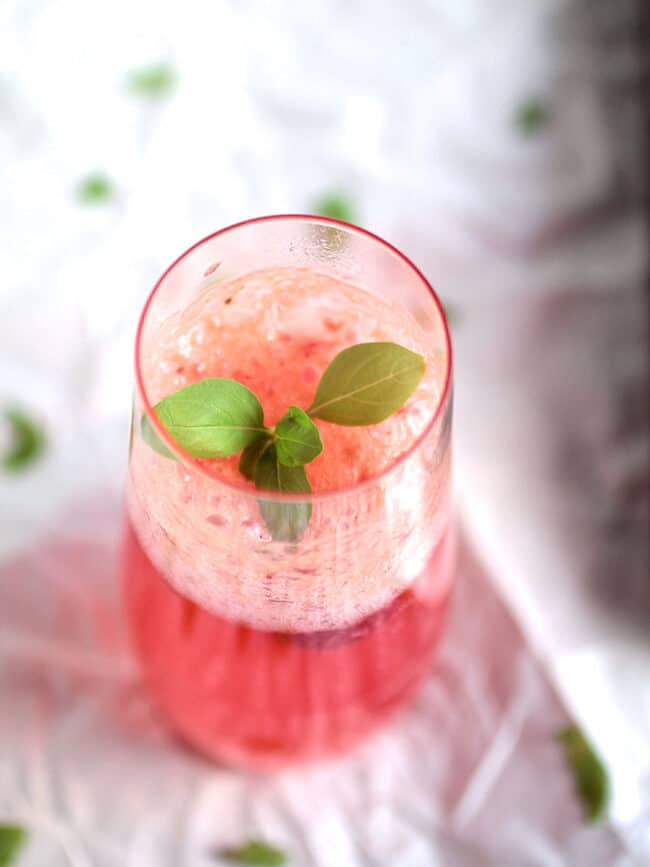 Close up of a sprig of fresh basil in a champagne glass filled with raspberry spritzer.