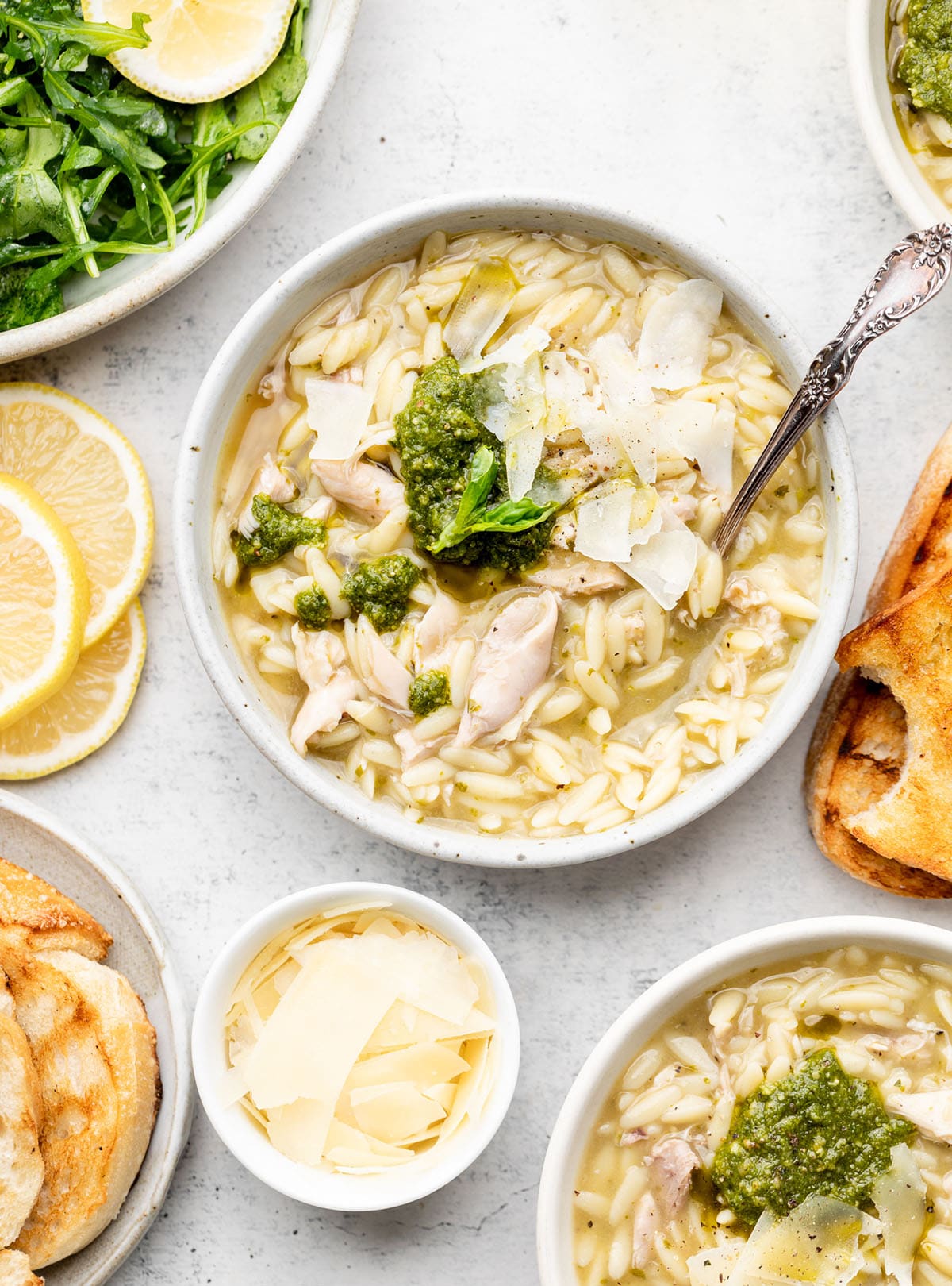 Chicken orzo soup in a white bowl, topped with a scoop of pesto.