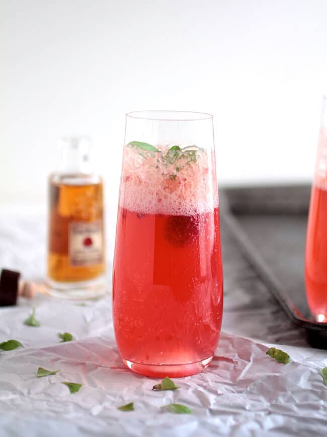 Raspberry basil bourbon spritzer in a champagne glass with a white background.