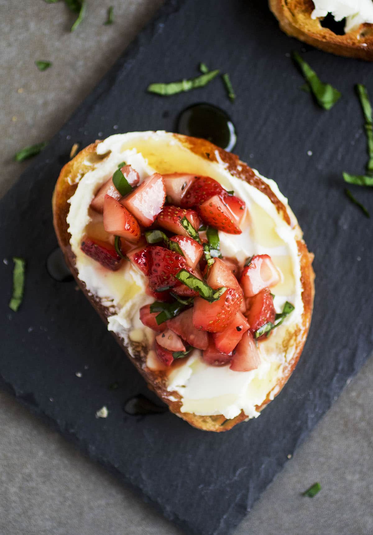Crostini on a slate platter topped with strawberries and fresh basil.