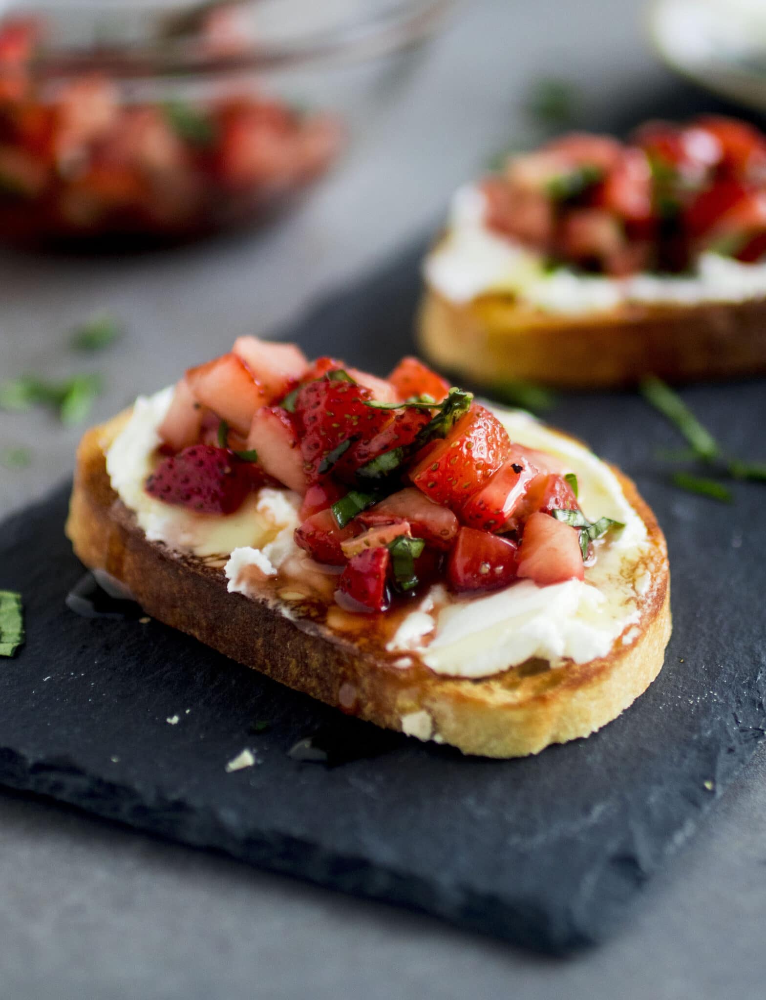 Crostini topped with goat cheese and strawberry basil salsa, sitting on a slate platter.
