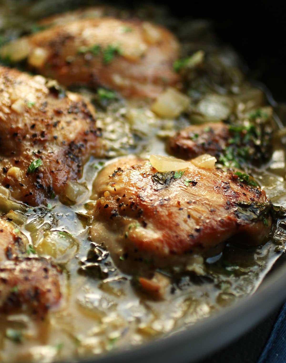 Chicken thighs in a skillet with broth and spinach.
