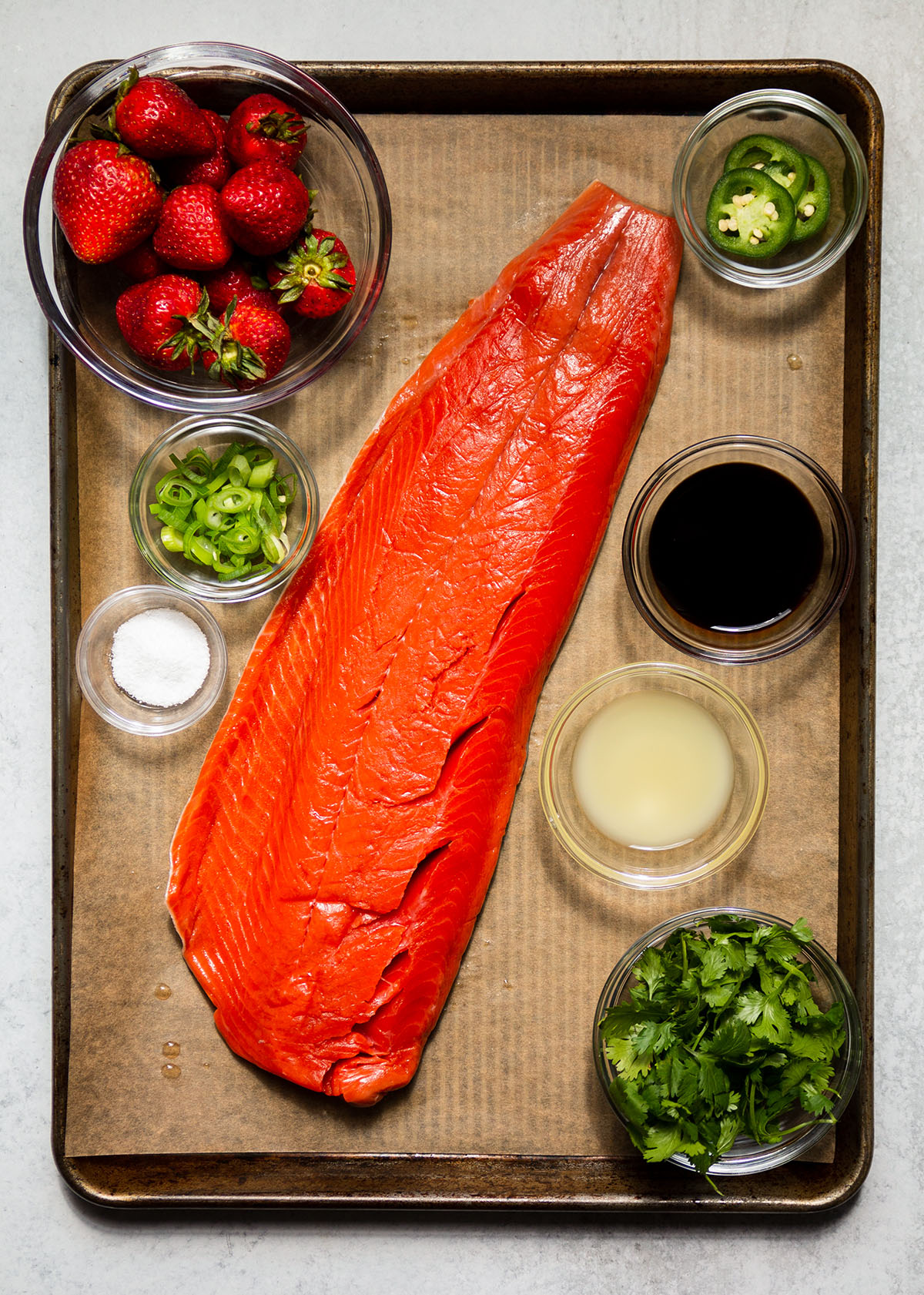 Salmon fillet on a sheet pan surrounded by salsa ingredients.