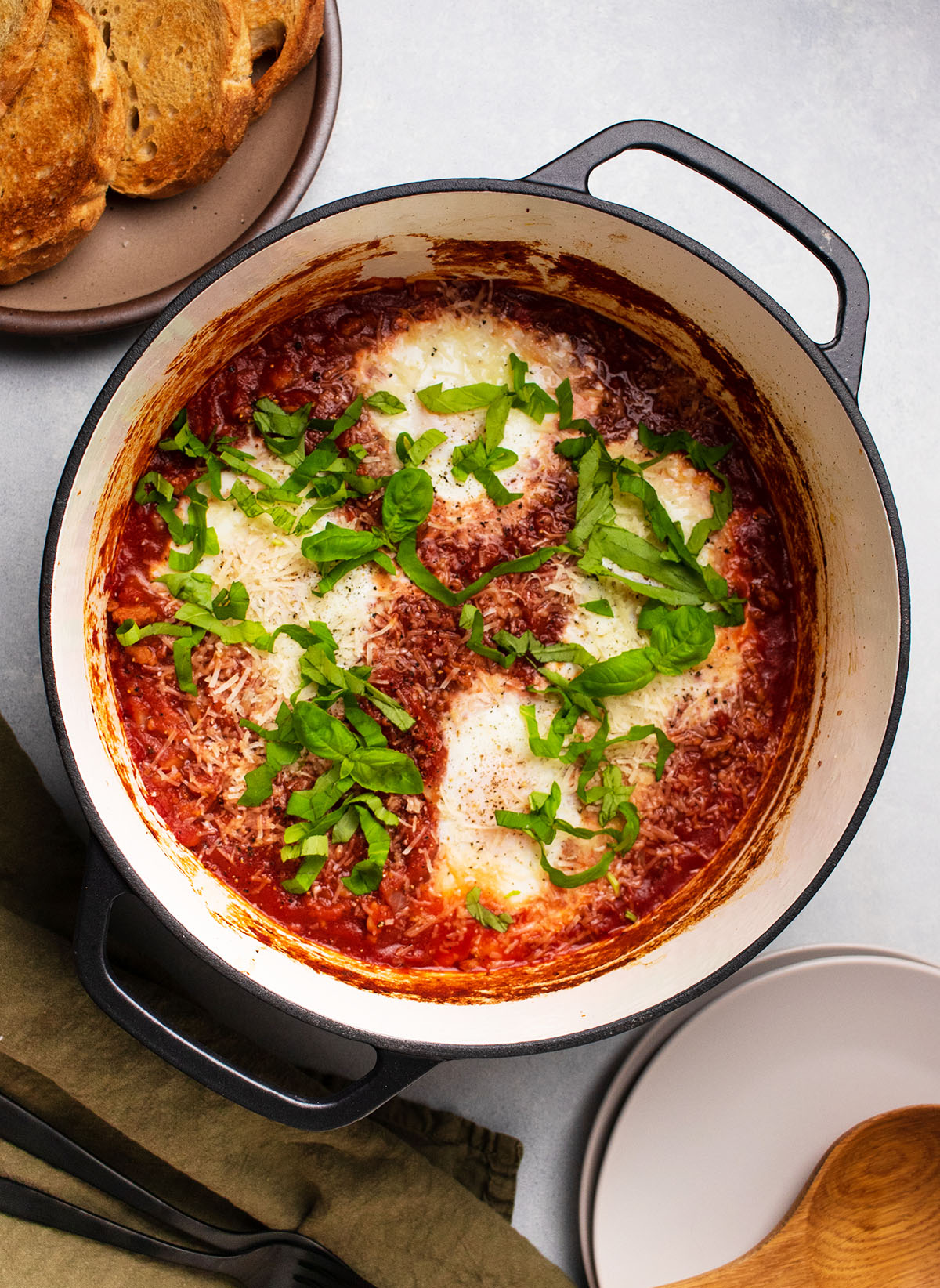 Large pot filled with tomato sauce and baked eggs, topped with fresh basil.