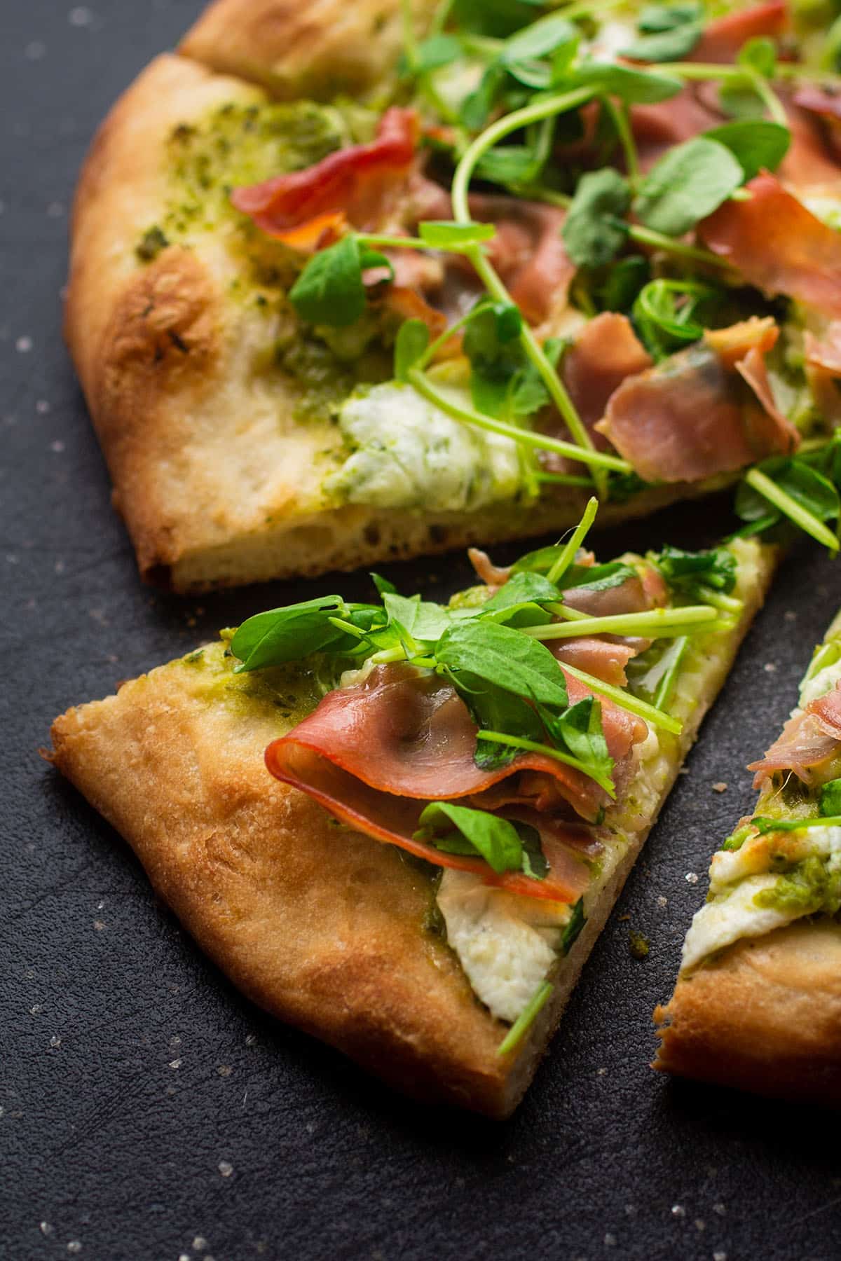 A slice of pea shoot pizza on a black cutting board.