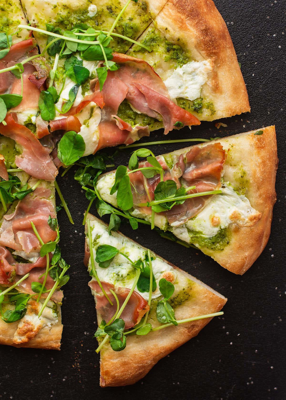 Slices of pea shoot pizza on a black cutting board.