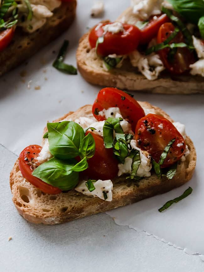 Close up of toasted bread topped with warm bruschetta and fresh basil leaves.