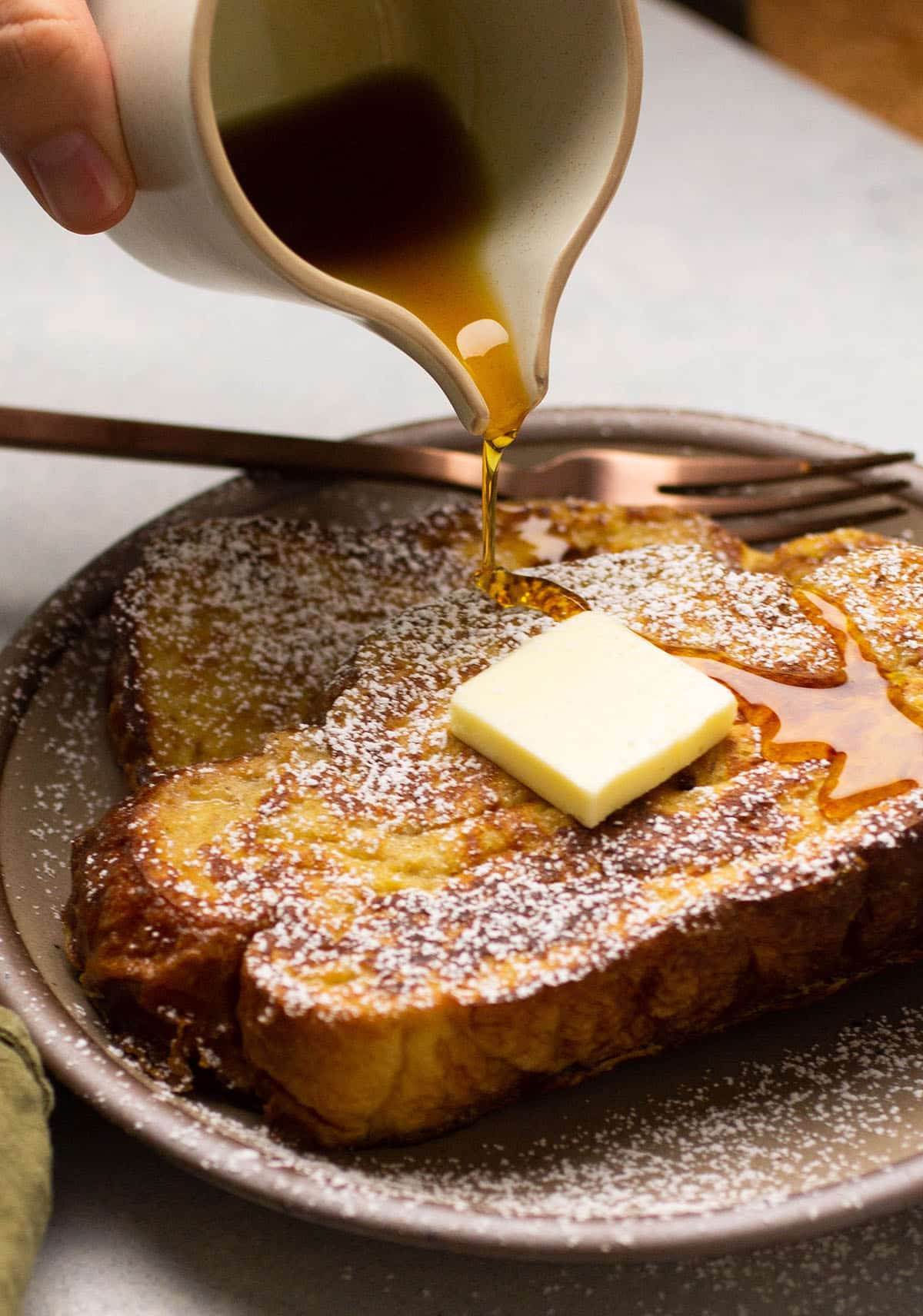 Hand pouring maple syrup over french toast slices.