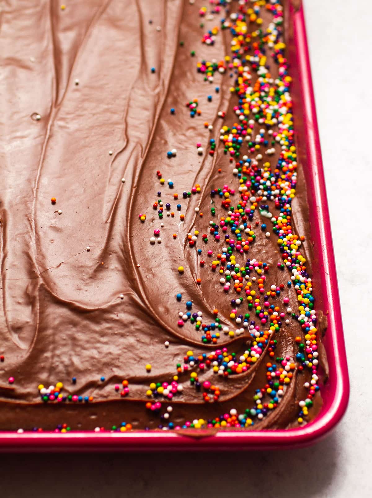 Chocolate sheet cake with sprinkles in a pink pan.
