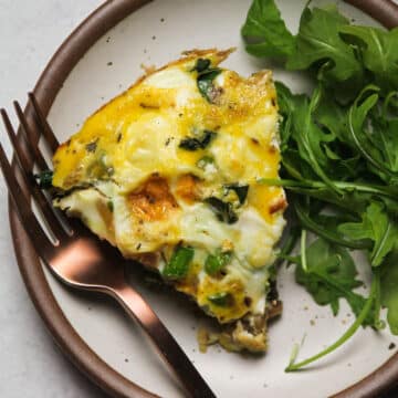 Slice of frittata on a white plate with a copper fork.