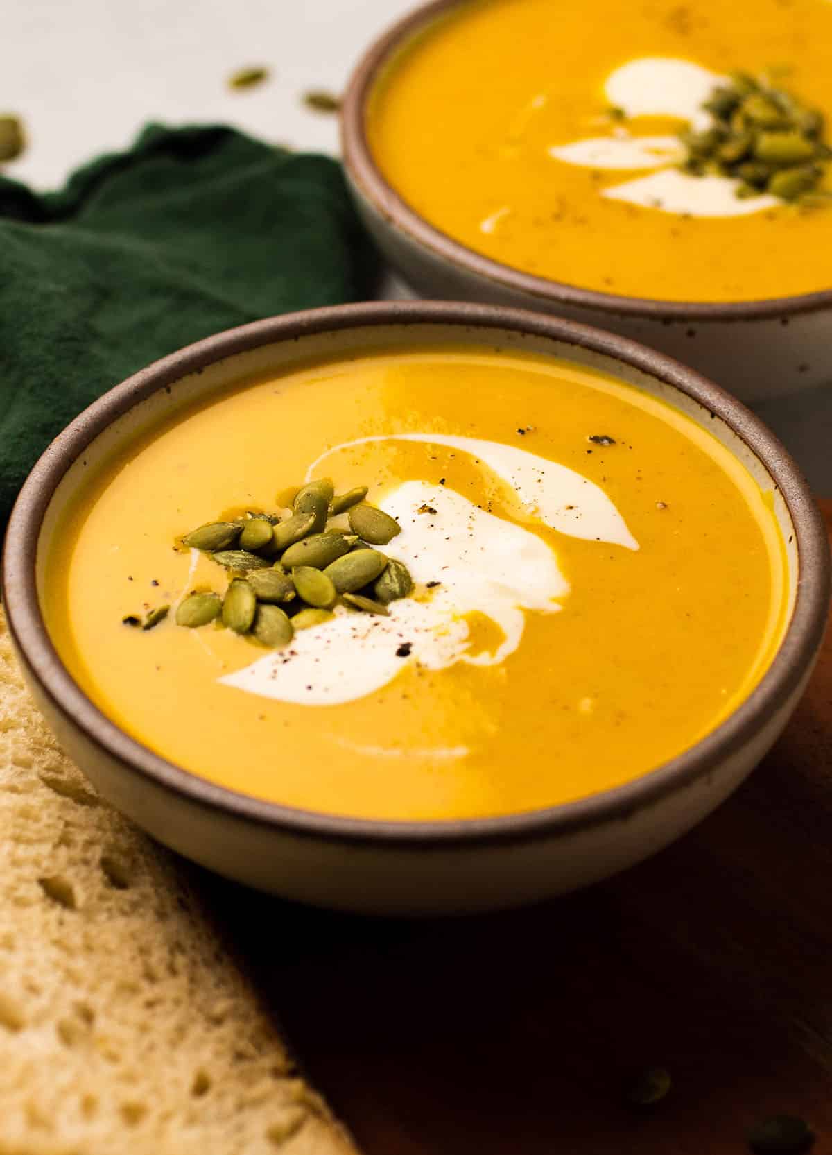 Curried squash soup in a shallow ceramic bowl, topped with pumpkin seeds and creme fraiche.