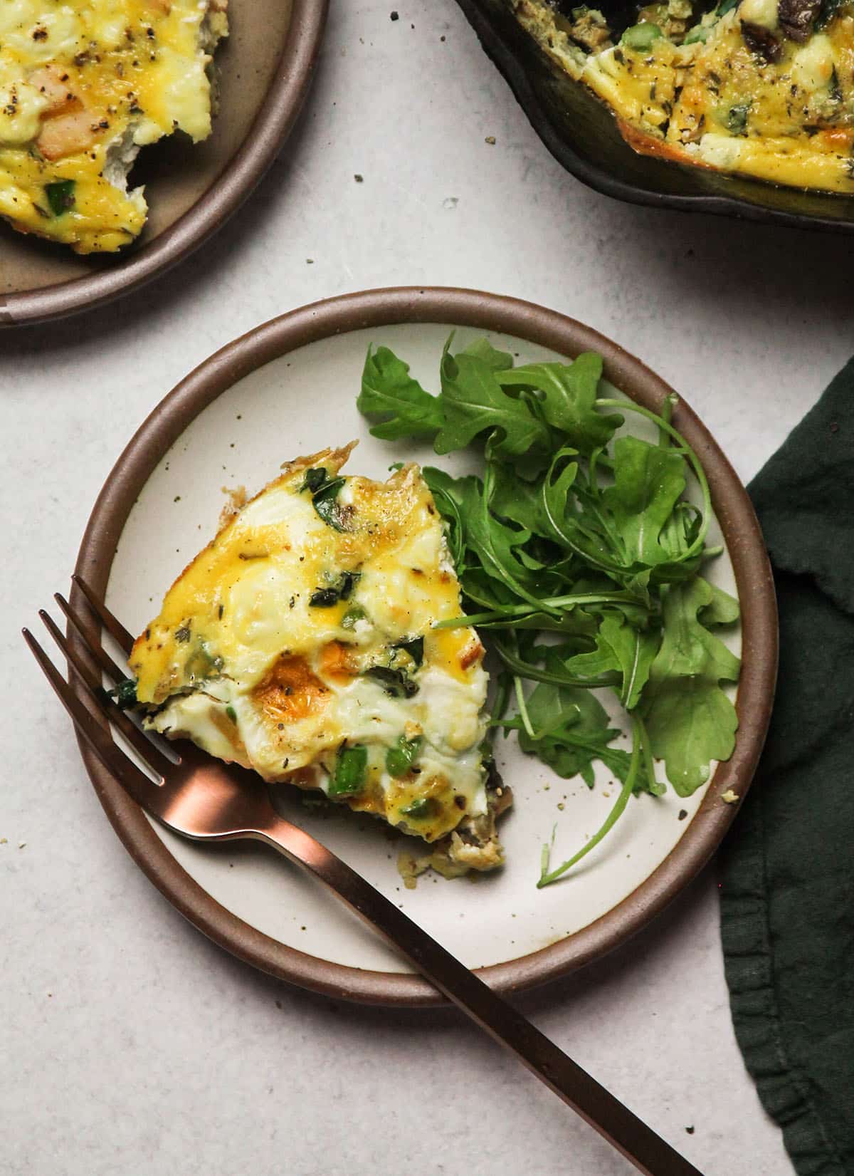 Frittata slice on a small white plate with arugula salad.