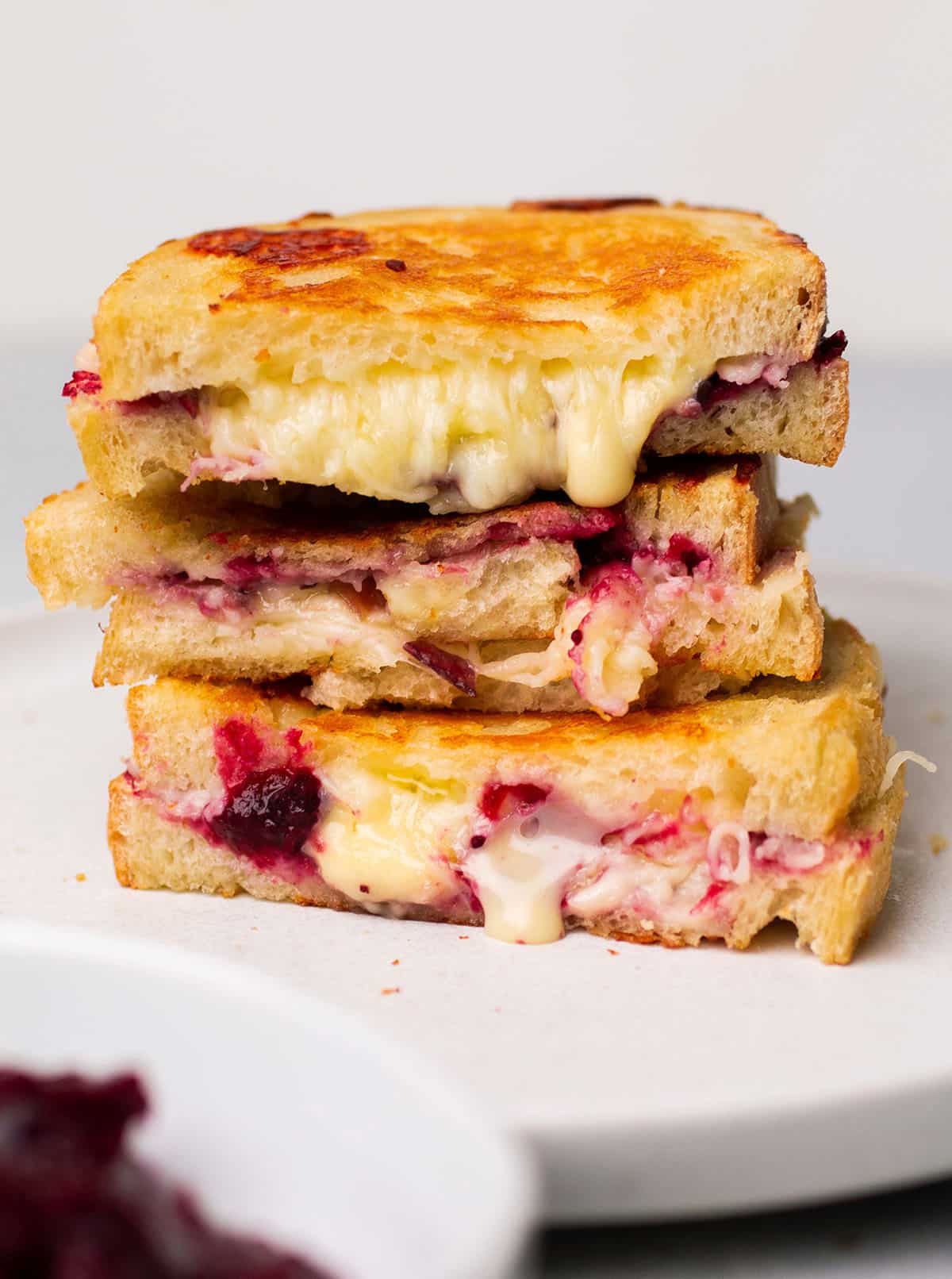 Three cranberry grilled cheese sandwiches, stacked on top of each other on a white plate.