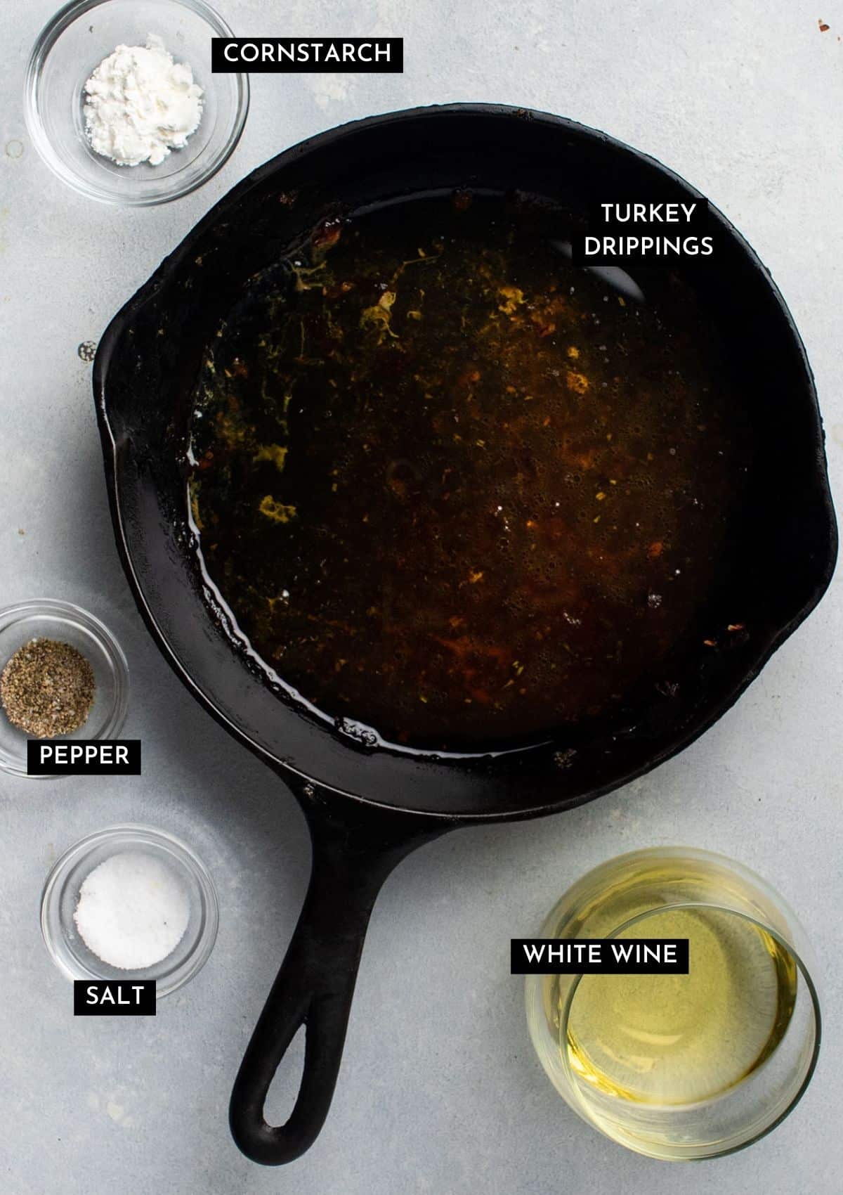 Turkey drippings in a cast iron skillet next to a glass of white wine and various seasonings.