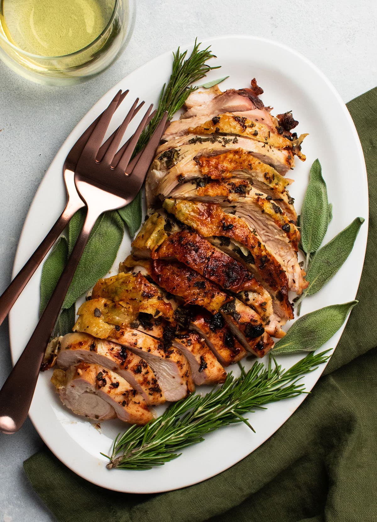 Sliced turkey breast on a large white platter with fresh herbs.