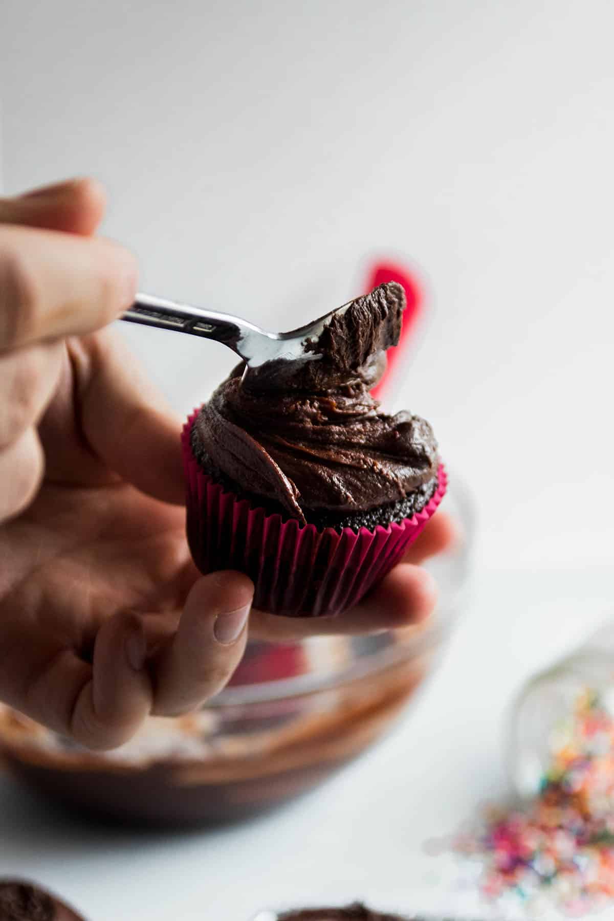 Hands using a small spoon to spread frosting over a cupcake.