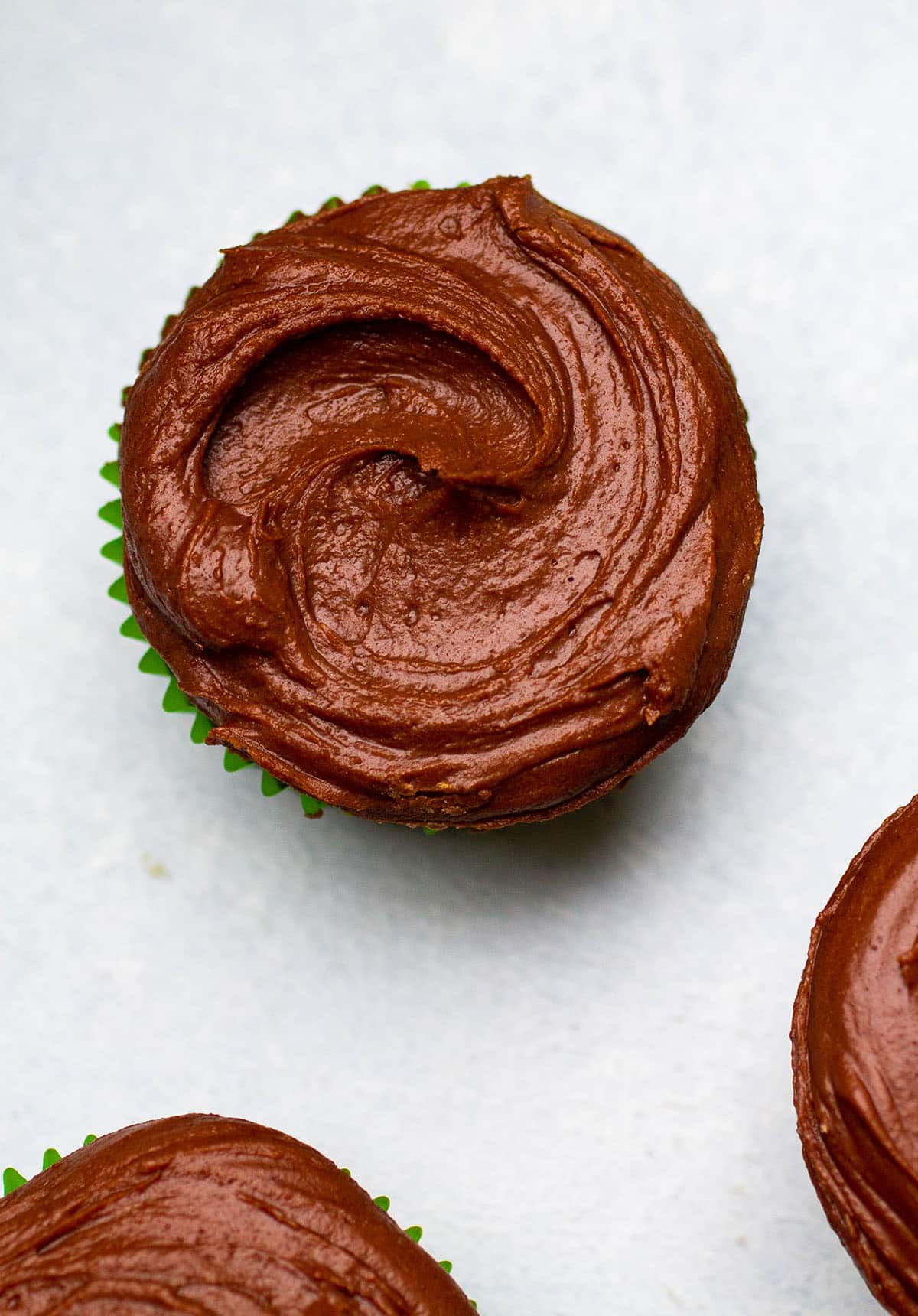Three cupcakes topped with chocolate frosting on a white table.