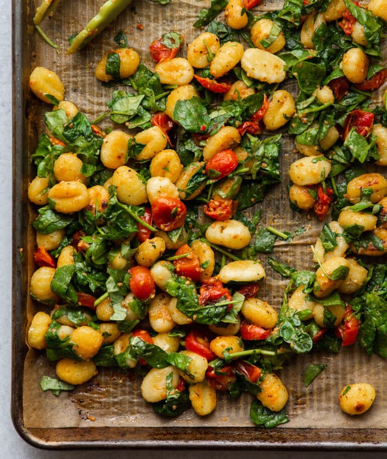 Gnocchi and tomatoes on a sheet pan with fresh spinach.