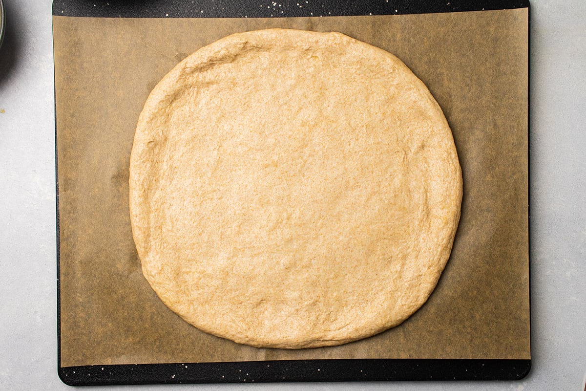 Whole wheat pizza dough, stretched into shape on a piece of parchment paper.